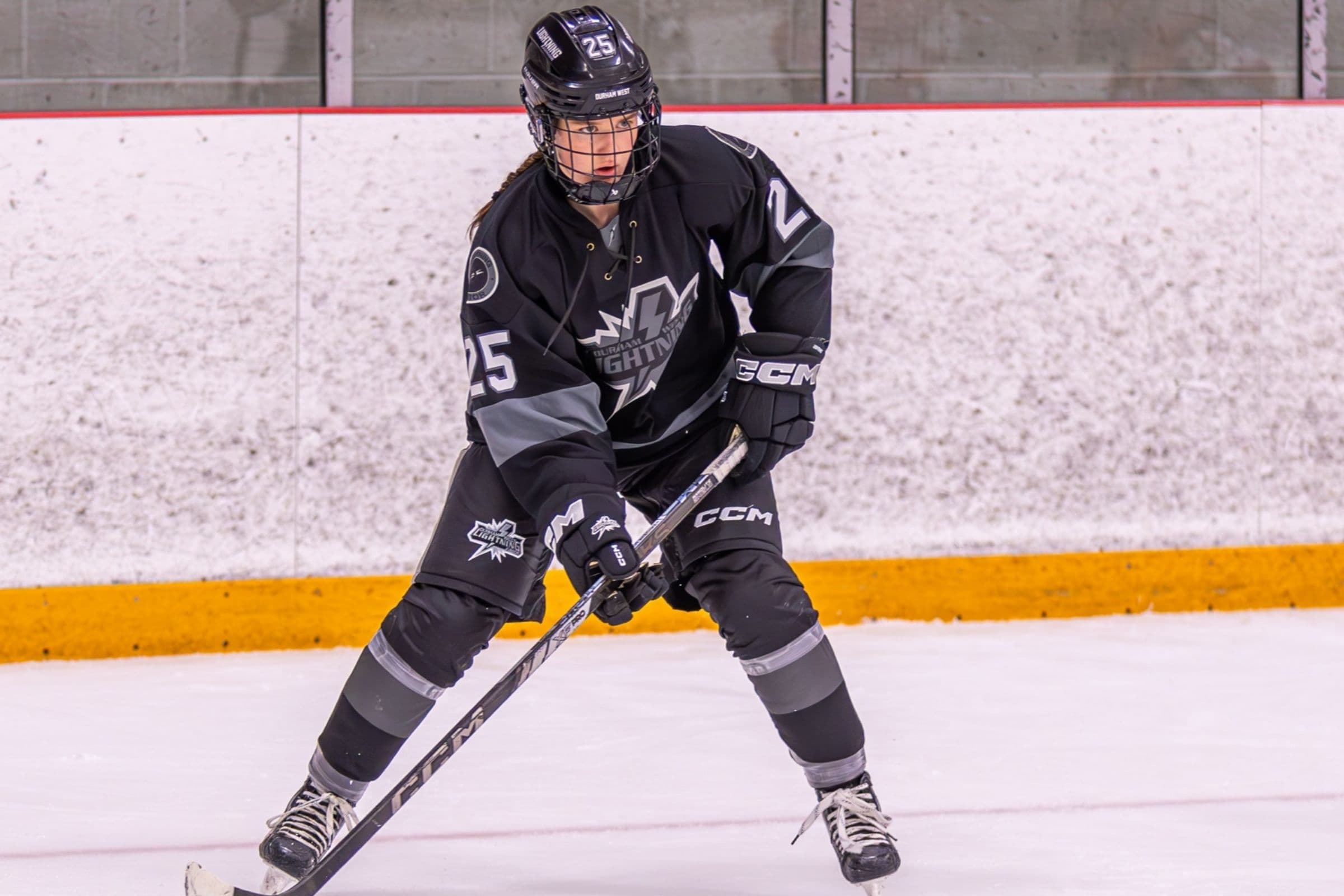 Durham West Junior Lightning player number 25 crouches over the puck in the black jersey