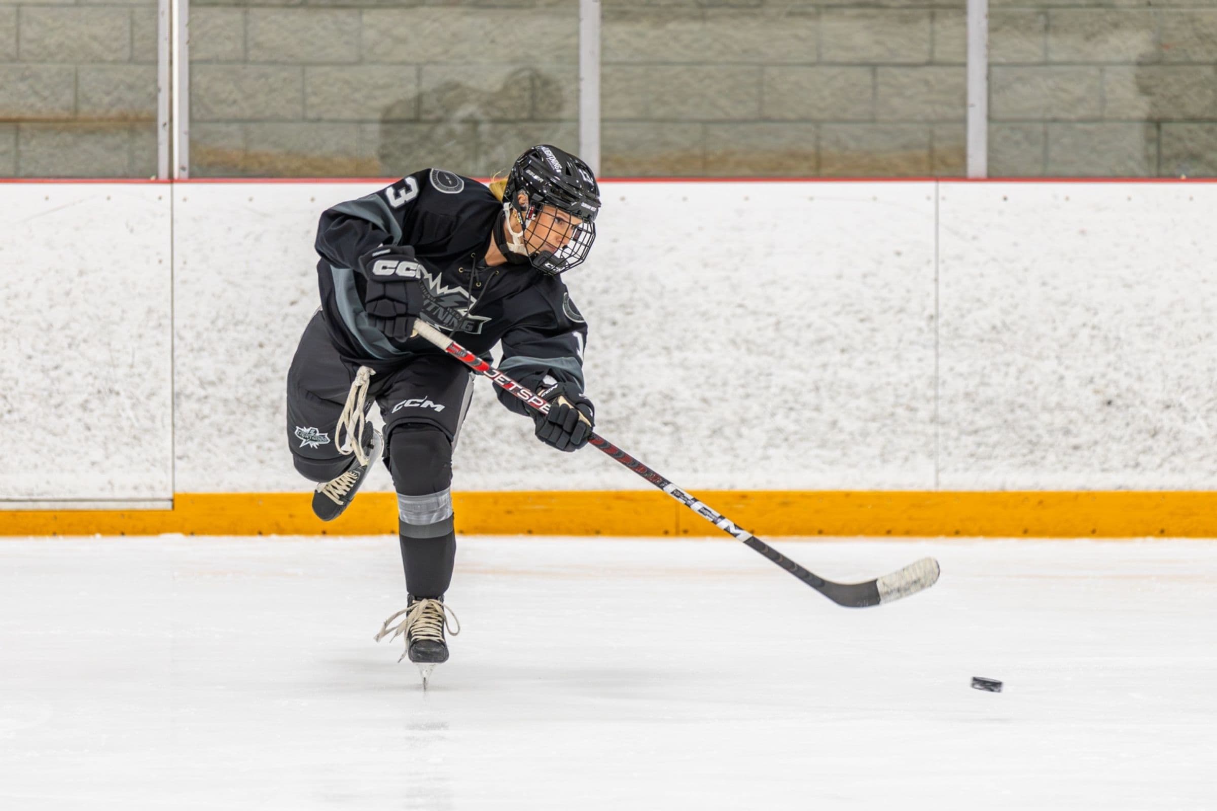 Lightning player number 3 follows through on a shot in the black jersey as the puck skims away