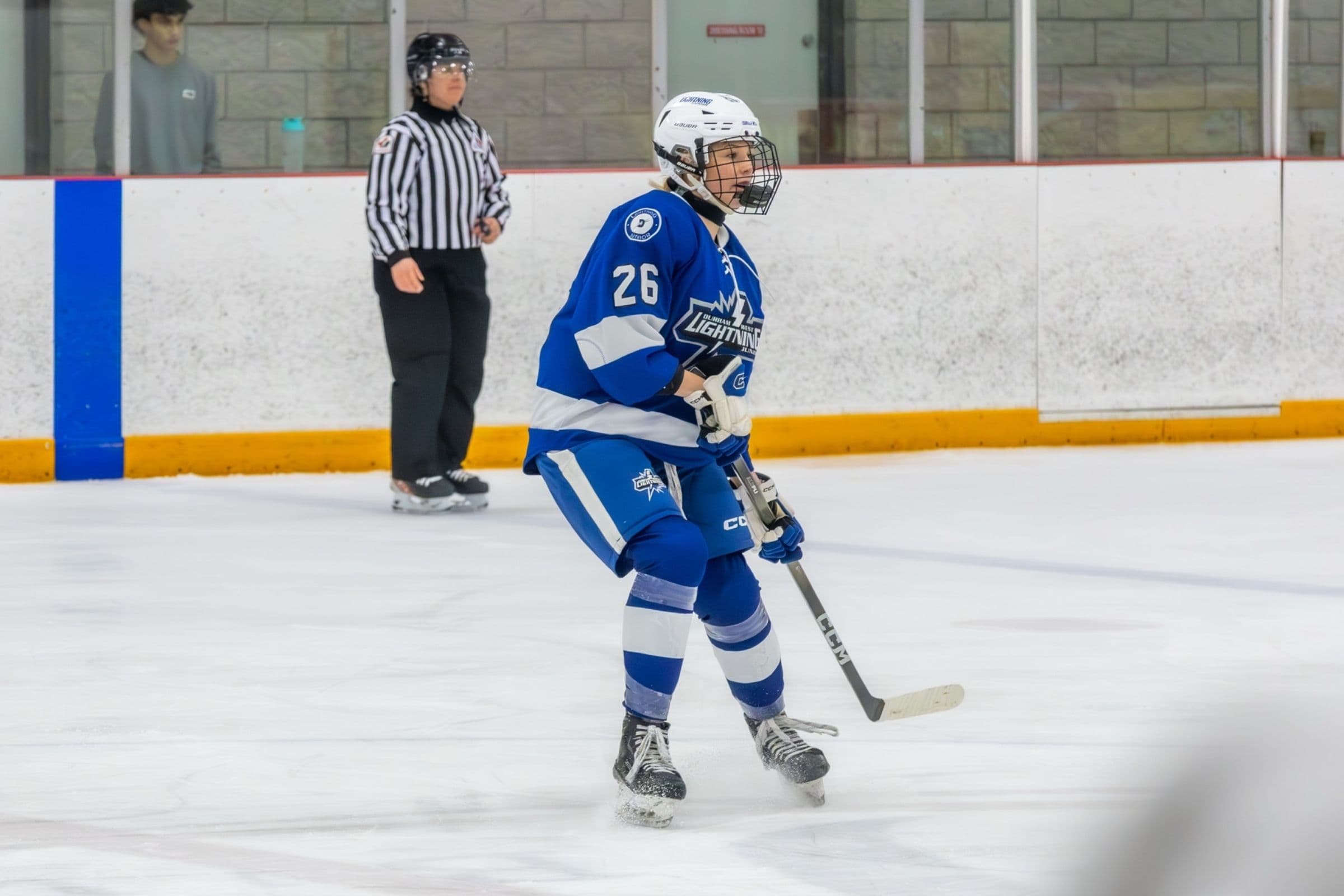 Lightning player number 26 skates up the ice in the blue home jersey as a referee looks on