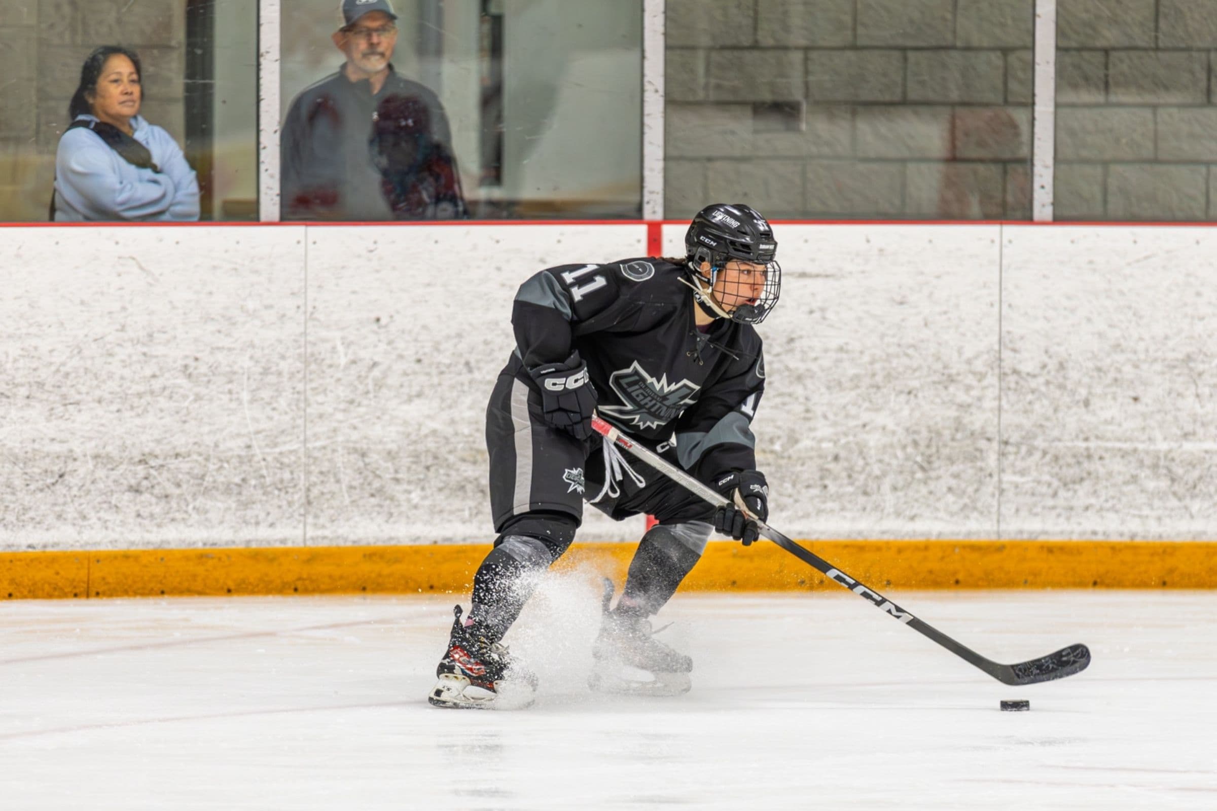 Lightning player number 11 drives through the slot in the black jersey, kicking up snow as fans watch